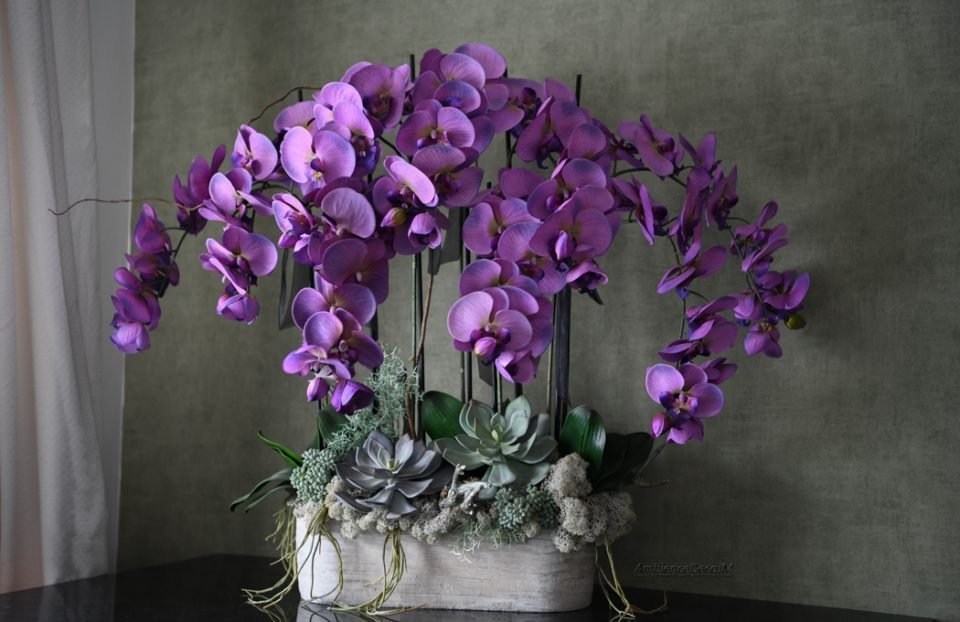 Large luxury artificial orchid arrangement featuring cascading purple silk Phalaenopsis orchids, realistic succulents, moss accents, and contemporary styling in a modern planter. Statement floral centrepiece measuring 71cm high and 86cm wide.