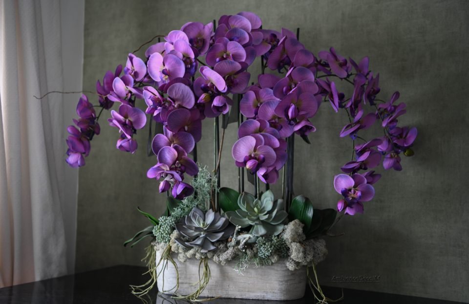 Large luxury artificial orchid arrangement featuring cascading purple silk Phalaenopsis orchids, realistic succulents, moss accents, and contemporary styling in a modern planter. Statement floral centrepiece measuring 71cm high and 86cm wide.